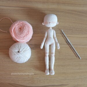 May include: A white crocheted doll with pink yarn and two crochet hooks on a wooden surface. The doll is missing its eyes and mouth. The text '@stitcheshandmade' is visible in the bottom left corner of the image.