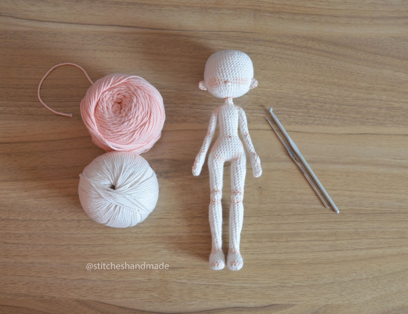 May include: A white crocheted doll with pink yarn and two crochet hooks on a wooden surface. The doll is missing its eyes and mouth. The text '@stitcheshandmade' is visible in the bottom left corner of the image.