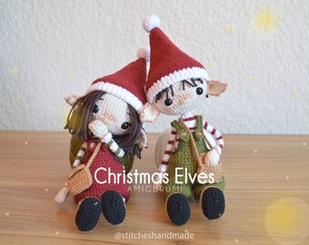 May include: Two handmade crochet Christmas elves. One elf wears a red dress and the other wears green overalls. Both elves have red Santa hats with white trim and small tan purses. The text "Christmas Elves AMIGURUMI" is visible.
