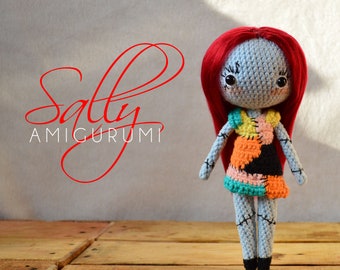 May include: A crocheted amigurumi doll of Sally from The Nightmare Before Christmas. She has red hair, a blue dress with colorful patches, and black eyes. The doll is standing on a wooden surface.