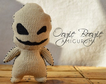 May include: A crocheted amigurumi toy of Oogie Boogie from the movie The Nightmare Before Christmas. The toy is beige with black eyes and a black mouth. The toy is standing on a wooden surface. The text "Oogie Boogie Amigurumi" is written in black cursive on a white background.