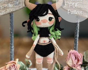 May include: Crocheted amigurumi doll representing the zodiac sign Taurus. The doll has green hair, black and brown clothing, and a light pink face. The doll is standing on a wooden surface with a sign that reads "Taurus PDF Pattern".