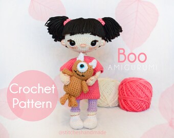 May include: A crocheted doll of the character "Boo" from Monsters, Inc., wearing a pink dress and holding a brown monster plushie. The doll has black yarn hair and is labeled "Boo Amigurumi" and "Crochet Pattern".