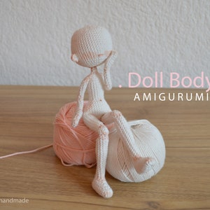 May include: White crocheted amigurumi doll body sitting on two balls of yarn, one pink and one white. The doll is sitting with its legs crossed and its right hand on its cheek. The text "Doll Body. AMIGURUMI" is written in pink letters on a white background.