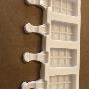 May include: White plastic popsicle mold with four individual compartments. Each compartment has a grid pattern and a handle on the side.
