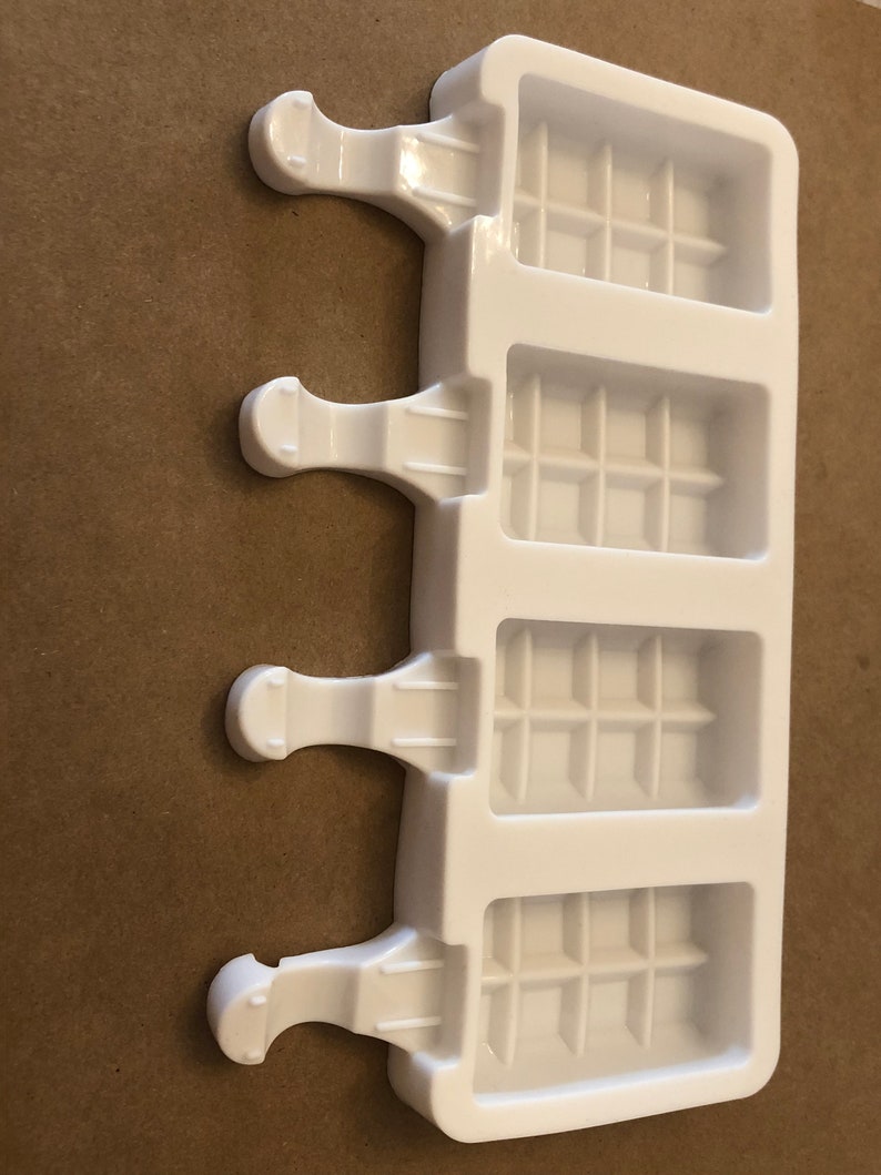 May include: White plastic popsicle mold with four individual compartments. Each compartment has a grid pattern and a handle on the side.