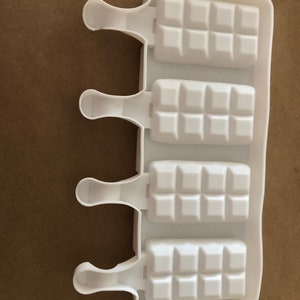 May include: White silicone popsicle mold with four individual molds, each with a rectangular shape and a textured surface. Each mold has a handle for easy removal.