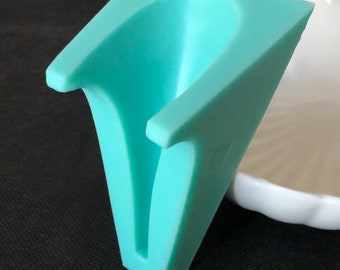 May include: A light blue silicone mold shaped like a V with a rounded top. The mold is designed for making a cake or other dessert.