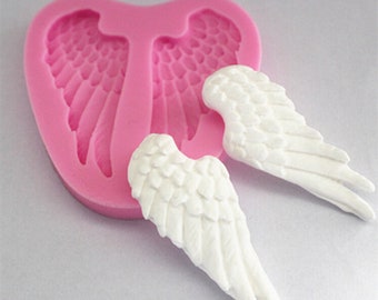 May include: Pink silicone mold with two white angel wings. The mold is shaped like a heart and has a detailed design of angel wings.