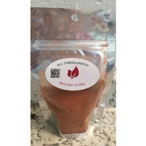 May include: A silver resealable pouch with a white oval label that says "ALL THINGS EARTHY RED DIRT STORE" with a red leaf logo. The pouch contains a red powder.