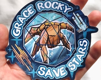 Op de afbeelding: Een sticker met een blauwe rand en de woorden "Grace Rocky Save Stars". De sticker heeft een geometrisch ontwerp met een bruine figuur in een blauw-witte kristalachtige vorm. Extra blauwe steraccenten zijn inbegrepen.
