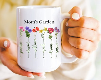 May include: White ceramic mug with the text "Mom's Garden" and a floral design with names written on the stems. The names are Jennifer, David, William, April, Brian, and Susan.
