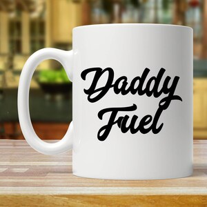 May include: White ceramic coffee mug with a black inscription that reads "Daddy Fuel".