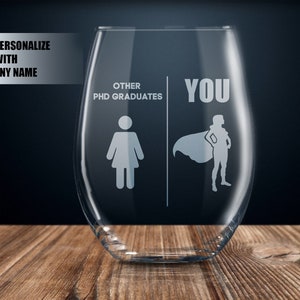 Op de afbeelding: Een helder glazen wijnglas met de tekst "Other PhD Graduates" aan de linkerkant en "You" aan de rechterkant. De linkerkant toont een silhouet van een persoon, terwijl de rechterkant een silhouet van een persoon met een cape toont.