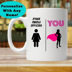 May include: White ceramic coffee mug with a black silhouette of a woman on the left side and the text "Other Parole Officers". On the right side is a black silhouette of a woman wearing a pink cape and the text "YOU" with pink rhinestones.