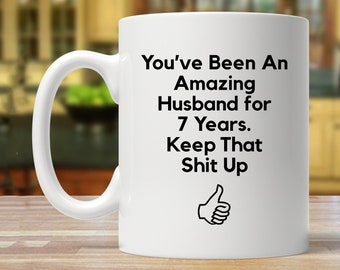 May include: White ceramic coffee mug with black text that reads "You've Been An Amazing Husband for 7 Years. Keep That Shit Up" and a thumbs up icon.