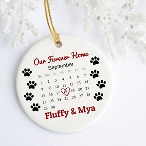 May include: White ceramic ornament with a calendar for September, a red heart around the 18th, and the text "Our Furever Home" and "Fluffy & Mya".