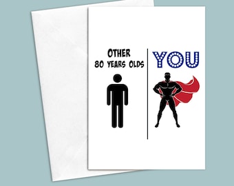 May include: A greeting card with a black and white stick figure illustration of a person labeled "Other 80 Years Olds".  Next to it is a black silhouette of a superhero with a red cape labeled "YOU".