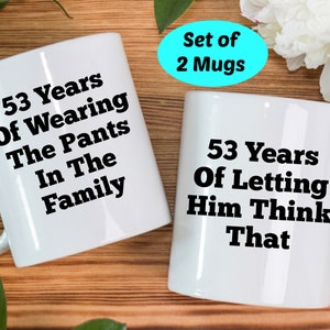 May include: Set of two white ceramic mugs with black text. One mug reads "53 Years Of Wearing The Pants In The Family". The other mug reads "53 Years Of Letting Him Think That".