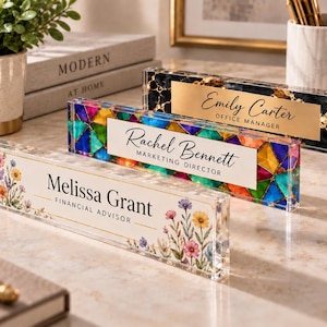 May include: Three rectangular acrylic desk nameplates. The front one features a floral design with the text Melissa Grant Financial Advisor. The middle one has a stained-glass pattern with the text Rachel Bennett Marketing Director. The back one has a black marble and gold foil pattern with the text Emily Carter Office Manager.
