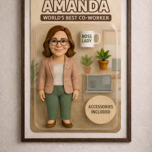 Pu&ograve; includere: Una figura da collezione incorniciata di una donna di nome Amanda, etichettata come "La migliore collega del mondo". La figura indossa un blazer rosa, pantaloni verdi e occhiali. Gli accessori includono una tazza con la scritta "BOSS LADY", piante e un laptop.