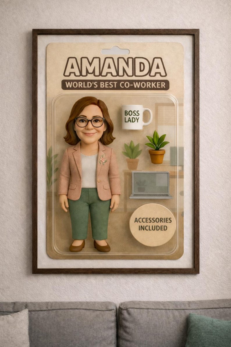Pu&ograve; includere: Una figura da collezione incorniciata di una donna di nome Amanda, etichettata come "La migliore collega del mondo". La figura indossa un blazer rosa, pantaloni verdi e occhiali. Gli accessori includono una tazza con la scritta "BOSS LADY", piante e un laptop.