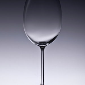 May include: A clear glass wine glass with a long stem and a round bowl. The glass is empty and is sitting on a reflective surface.