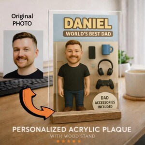 May include: A personalized acrylic plaque with a wood stand. The plaque features a bobblehead figure of a man, with the text "DANIEL WORLD'S BEST DAD". Accessories include a phone, mug, headphones, and a game controller.