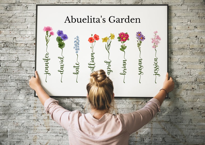 May include: A white framed print with the text "Abuelita's Garden" at the top.  The print features seven watercolor illustrations of flowers with names written underneath each flower: Jennifer, David, Kate, William, April, Brian, Susan, and Jessica.