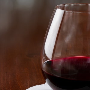 May include: A glass of red wine in a clear glass, sitting on a white napkin on a wooden table.