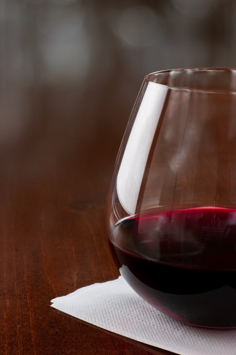 May include: A glass of red wine in a clear glass, sitting on a white napkin on a wooden table.
