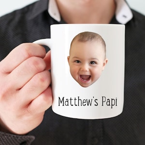 Puede incluir: Taza de cerámica blanca con una foto de la cara de un bebé y el texto "Matthew's Papi" impreso en ella.