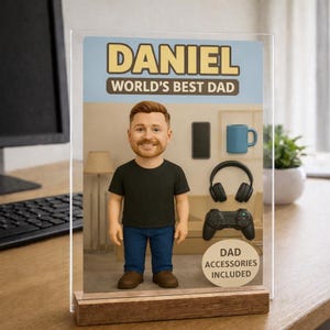 Puede incluir: Exhibici&oacute;n acr&iacute;lica personalizada con el texto "DANIEL WORLD'S BEST DAD". Muestra una figura de dibujos animados con camiseta negra y vaqueros azules, junto con un tel&eacute;fono, una taza azul, auriculares y un mando de juegos. Tambi&eacute;n se muestra "DAD ACCESSORIES INCLUDED".