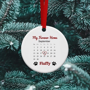 May include: White ceramic ornament with a red ribbon. The ornament has a calendar with the month of September highlighted and the text "My Furever Home" and "Fluffy".