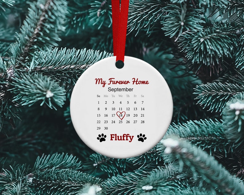 May include: White ceramic ornament with a red ribbon. The ornament has a calendar with the month of September highlighted and the text "My Furever Home" and "Fluffy".
