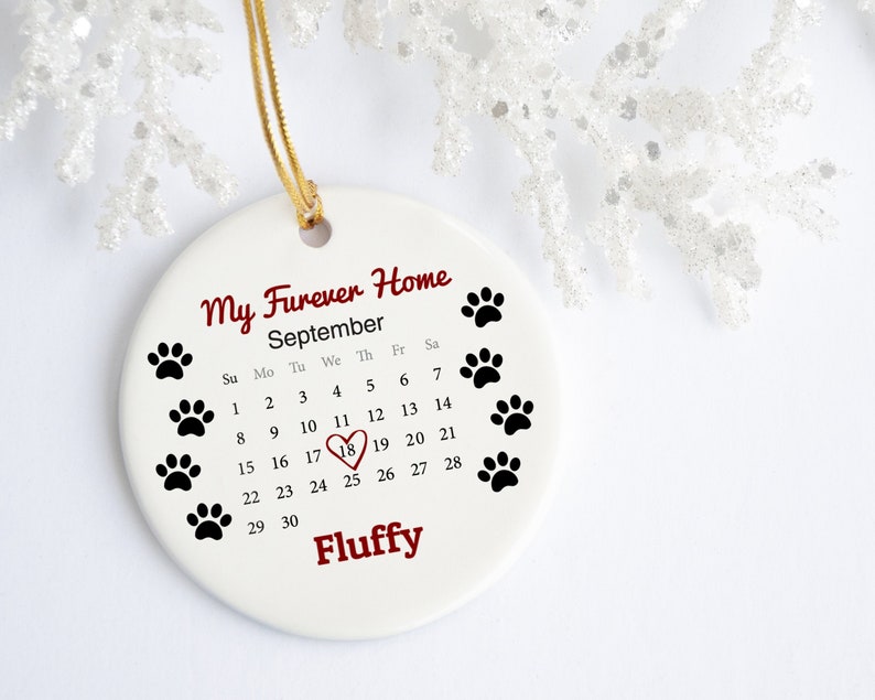 May include: White ceramic ornament with a calendar for September and the text "My Furever Home". The 18th is highlighted with a red heart. The ornament also has the name "Fluffy" and paw prints.