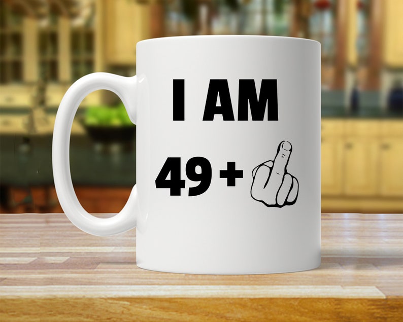 May include: White ceramic coffee mug with black text that reads "I AM 49+ " and a black and white illustration of a middle finger.