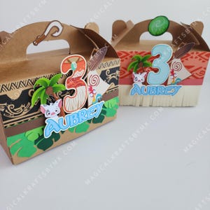 May include: Two brown favor boxes decorated with a Moana theme. The boxes have a handle and are decorated with a palm tree, a number 3, a character from the movie Moana, and the name Aubrey.