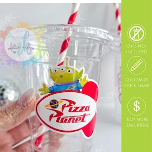 May include: A clear plastic cup featuring a sticker of a green three-eyed alien character and a red and white Pizza Planet logo. The cup includes a red and white striped straw. Text on the image includes STICKERS ONLY, CUPS NOT INCLUDED, CUSTOMIZE AGE & NAME, and BUY MORE SAVE MORE.