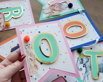 May include: A colorful banner with the letters "TWO" in gold and turquoise, with animal illustrations and confetti. The letters are decorated with gold trim.