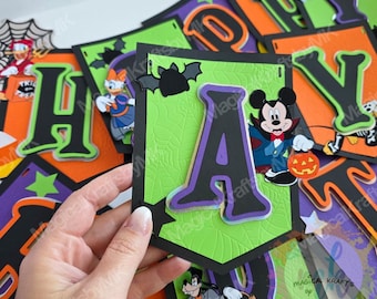 Puede incluir: Una pieza de banderín con temática de Halloween hecha de cartulina verde brillante con textura de telaraña. Una letra A negra grande con borde morado está centrada, decorada con un murciélago negro y un ratón vampiro sosteniendo una calabaza.