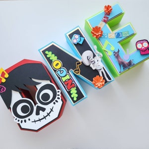 May include: One-letter, red, white, and black cardboard letter "O" decorated with a character from the movie Coco. The letter is part of a set of letters spelling "ONE" with each letter decorated with a different character from the movie Coco.