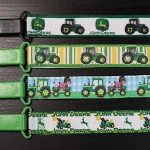 May include: Three green and black fabric clips with a John Deere tractor design. The top clip has a white background with green tractors and the text "John Deere". The middle clip has a yellow and green striped background with green tractors. The bottom clip has a blue and white checkered background with green tractors and the text "John Deere".