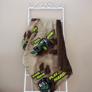 Puede incluir: Una manta de franela marrón y beige con un diseño de tractor verde y amarillo. La manta tiene el texto "I Dig Dirt", "Work Hard" y "Play Hard" en ella.