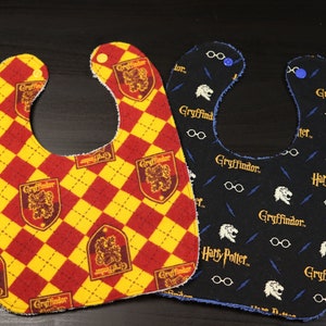 May include: Two baby bibs with a Harry Potter theme. One bib is red and yellow with a Gryffindor crest and the other is black with a Gryffindor crest and the words "Harry Potter" repeated.