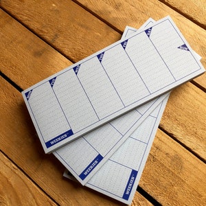 May include: Three white weekly planner pads with blue grid lines and the word "WEEKIES" printed in blue at the bottom. The days of the week are labeled at the top of each pad: Mon, Tue, Wed, Thu, Fri, Sat, Sun.