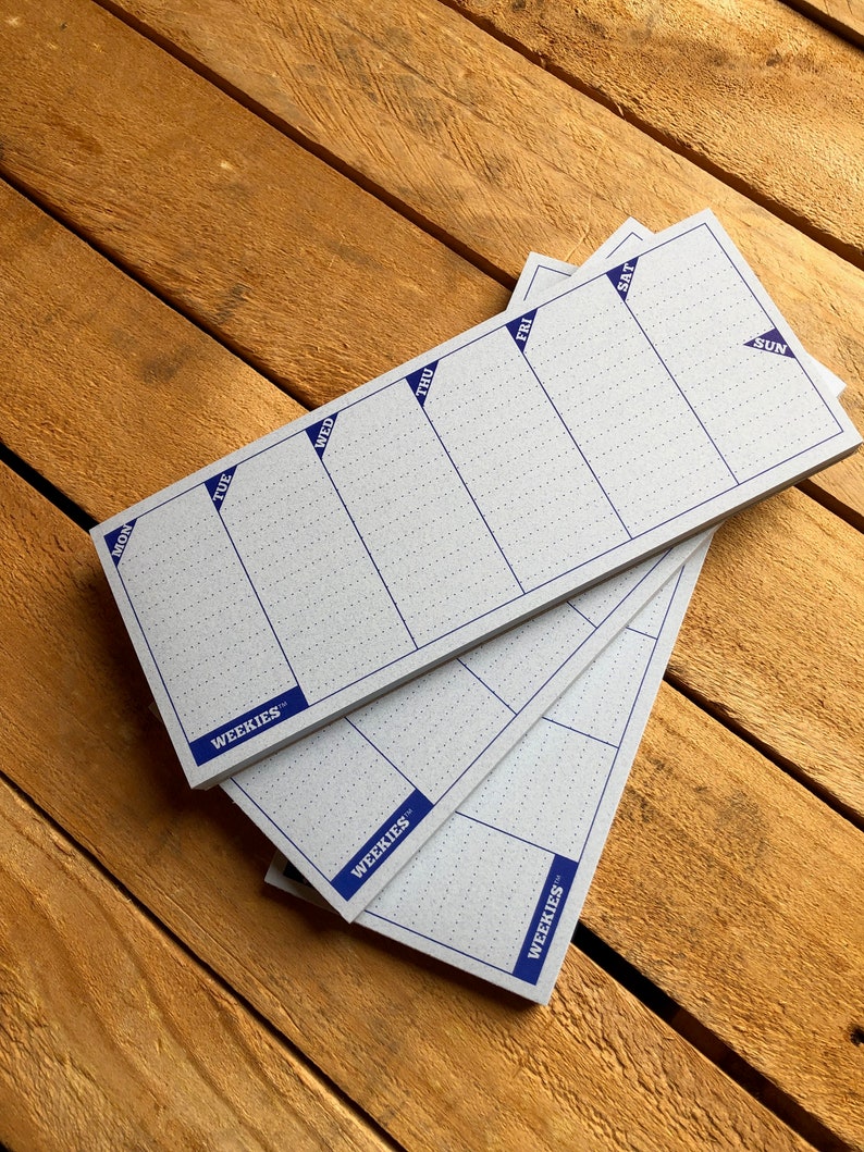 May include: Three white weekly planner pads with blue grid lines and the word "WEEKIES" printed in blue at the bottom. The days of the week are labeled at the top of each pad: Mon, Tue, Wed, Thu, Fri, Sat, Sun.