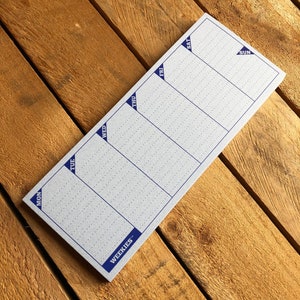 May include: A weekly planner notepad with a blue border and the word "WEEKIES" printed on the bottom. The notepad is divided into seven sections for each day of the week, labeled "MON", "TUE", "WED", "THU", "FRI", "SAT", and "SUN".