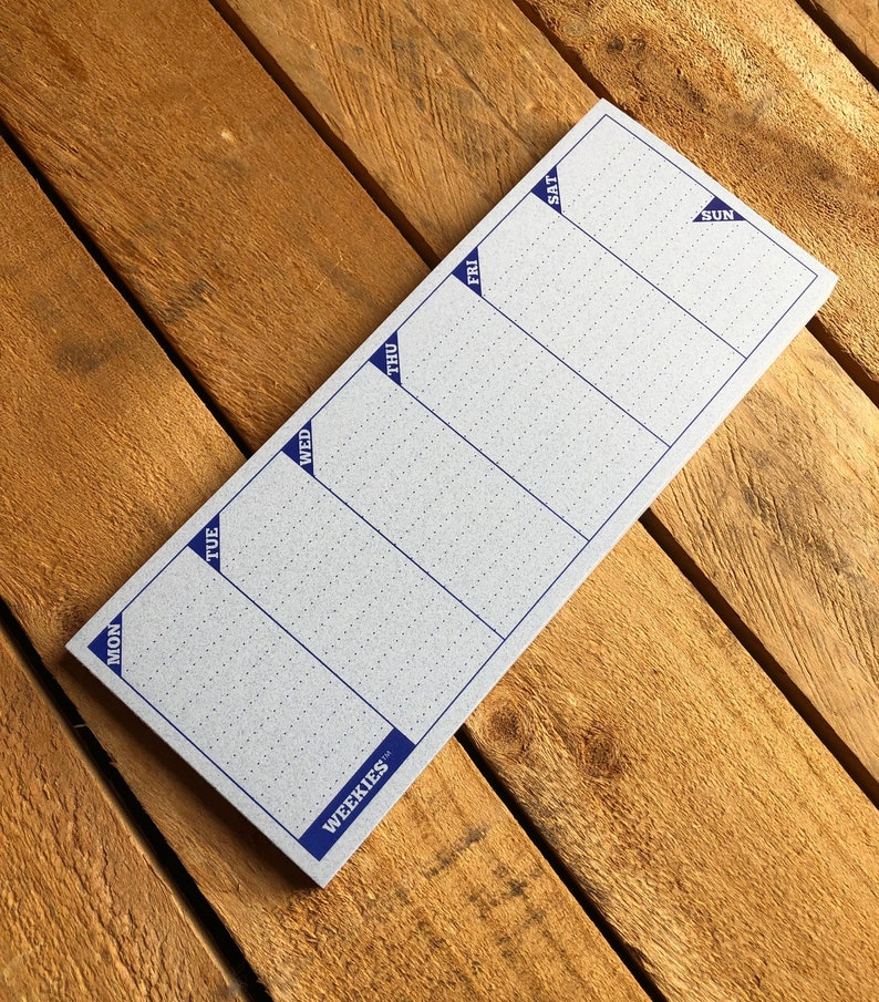 May include: A weekly planner notepad with a blue border and the word "WEEKIES" printed on the bottom. The notepad is divided into seven sections for each day of the week, labeled "MON", "TUE", "WED", "THU", "FRI", "SAT", and "SUN".