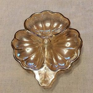 May include: A three-sectioned glass serving dish in the shape of a clover leaf. The dish is made of iridescent amber glass with a scalloped edge.